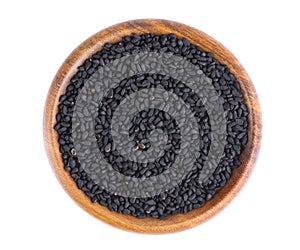 Black cumin seeds in wooden bowl, isolated on white background. Heap of black nigella seeds. Nigella sativa. Top view.