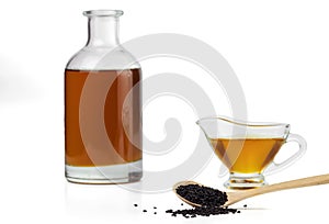 Black cumin seeds on a wooden spoon and black seed oil in a glass bottle and gravy boat.