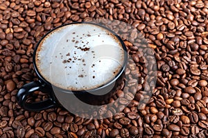 A black cup of black coffee with white froth is on the table where coffee beans are scattered. top shot copyspace