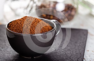 Black cup with ground coffee. Roasted coffee beans