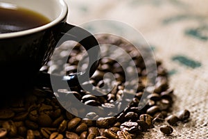 Black cup with handle, on a coffee sack with roasted beans around