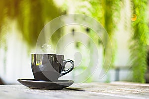 Black cup with steaming hot coffee on the wooden table