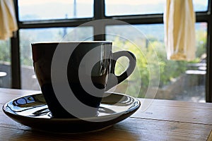 Black cup with steaming hot coffee on the wooden table with blurred green garden background