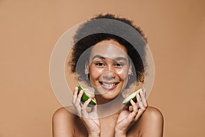 Black curly shirtless woman smiling while posing with avocado