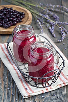 Black currant, greek yogurt, honey and lavender smoothie in glass with berries and flowers on background, vertical