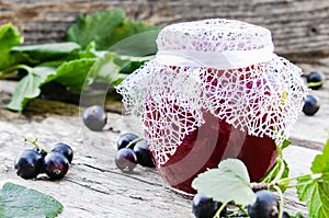 Black currant jam on the background of old boards near the green leaves and berries of currants. Natural currant jam