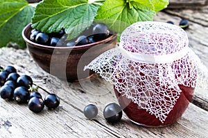 Black currant jam on the background of old boards near the green leaves and berries of currants. Natural currant jam