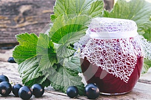 Black currant jam on the background of old boards near the green leaves and berries of currants. Natural currant jam