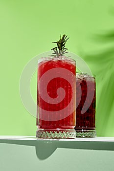 Black currant and raspberry lemonade drink over green background. White table with sunlight and palm leaf hard shadow. Summer,