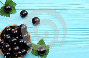 Black currant in wooden bowl with green leaf on blue wooden background