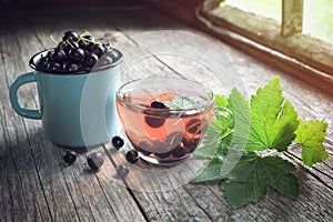 Black currants, glass cup of fruit tea with currant berries on wooden table.