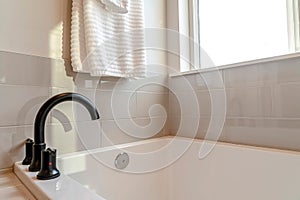 Black curved faucet and built in bathtub inside bathroom with white tile wall