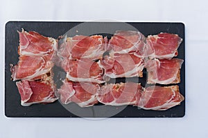 a black cutting board with slices of meat on it and a small knife