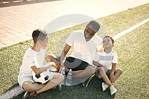 Black dad with his little cute sons are sitting on green grassy lawn