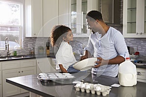 Black dad and young daughter look at each other while baking