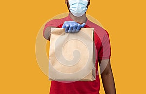 Black delivery man in medical mask and gloves holding package