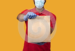 Black delivery man in medical mask and gloves holding package