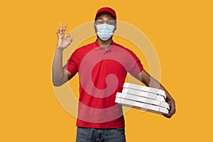 Black delivery man in medical mask holding pizza boxes