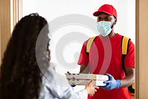 Black delivery man in medical mask holding pizza boxes