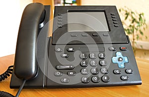 The black desktop push-button telephone. IP phone on desk in office