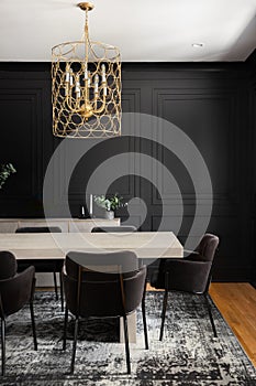 A black dining room with wainscoting walls and gold chandelier.