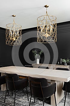 A black dining room with wainscoting walls and gold chandelier.