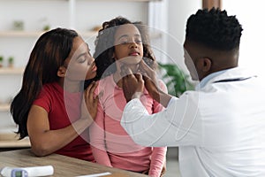 Black doctor palpating school girl throat at clinic