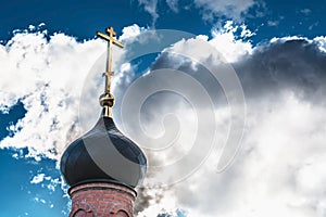 Black dome of the Church with a golden cross on the sky background with white clouds. tower of the old red brick in the light of t