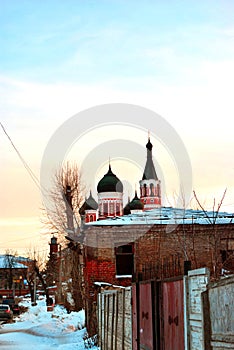 Black domes with crosses on top of orthodox church of red and white brick in winter evening landscape of residential