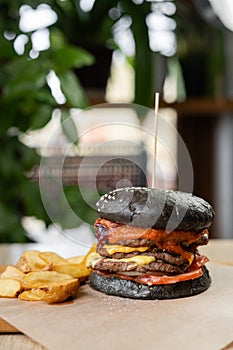 Black double burger served with fries on a wooden board on a table in a cafe. Fast food concept.