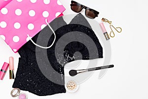 Black dress in a shopping bag and cosmetics on a white background. Flat lay