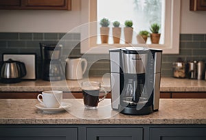 A black drip electric coffee machine with a glass teapot brews a morning drink. Household appliances, a white cup and a