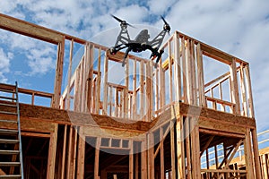 Black drone quadcopter with camera flying over residential construction home framing against