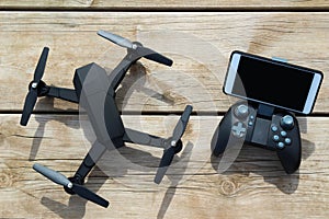 Black Drone quadcopter with a remote control and phone on wood table