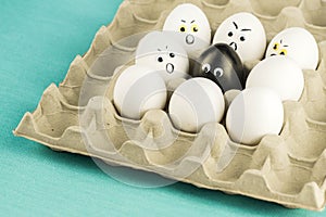 Black egg among angry, nervous, prejudiced eggs on paper tray. Xenophobia, racism concept.