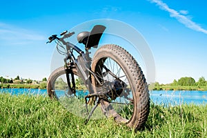 Black electric bike with thick wheels on the grass near the lake. Fatbike