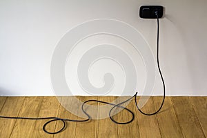 Black electric cable in wall socket on wooden parquet floor