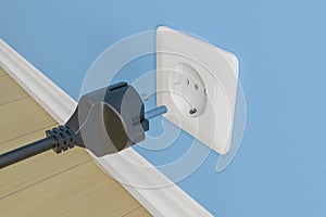 Black electric plug with cable near the socket. On blue wall background