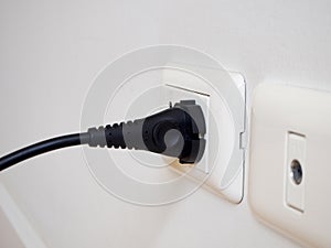 Black electric power plug on white socket on white wall