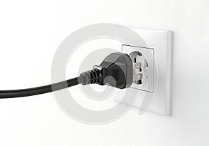 Black electrical plug inserted into a white wall socket