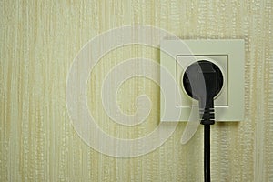 Black electrical plug in a white plastic socket on the wall