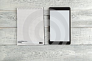 Black electronic tablet and paper notebook on vintage shabby white wooden background. the view from the top. flat lay