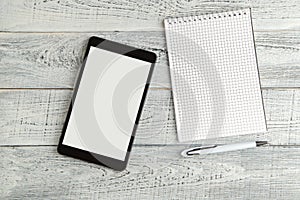 Black electronic tablet and paper notebook on vintage shabby white wooden background. the view from the top. flat lay