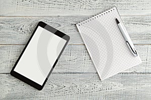 Black electronic tablet and paper notebook on vintage shabby white wooden background. the view from the top. flat lay