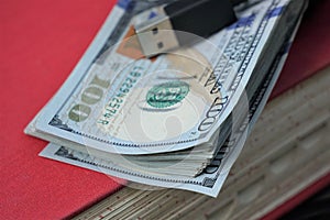 Stack of hundred dollar bills with USB cable on red book