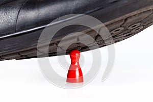 Black elegant shoe stomping and crushing a small little red pawn game piece under heel, closeup. Big vs small, danger, tension