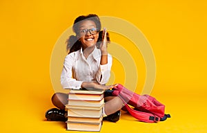 Black Elementary School Girl Raising Hand Sitting At Book Stack