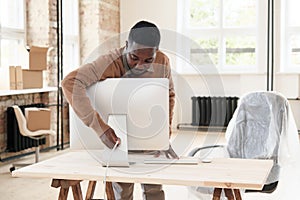 Black employee powering up computer in new office