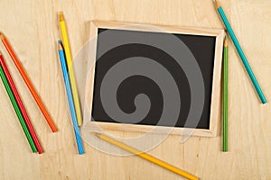 Black, empty, blank chalkboard with colored pencils on brown wooden desk flat lay from above