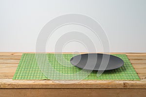 Black empty plate and bamboo placemat on wooden table. Chinese kitchen or restautant concept background